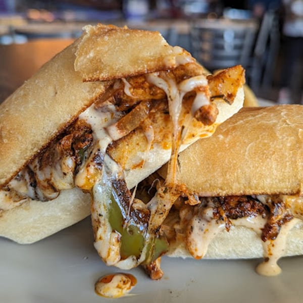 Two cheesy Rep's Place cheesesteak sandwiches with melted cheese and green peppers on a white plate.