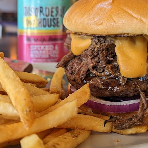 Close-up of a Rep's Place burger with pulled pork, melted cheese, red onion, and a side of fries.